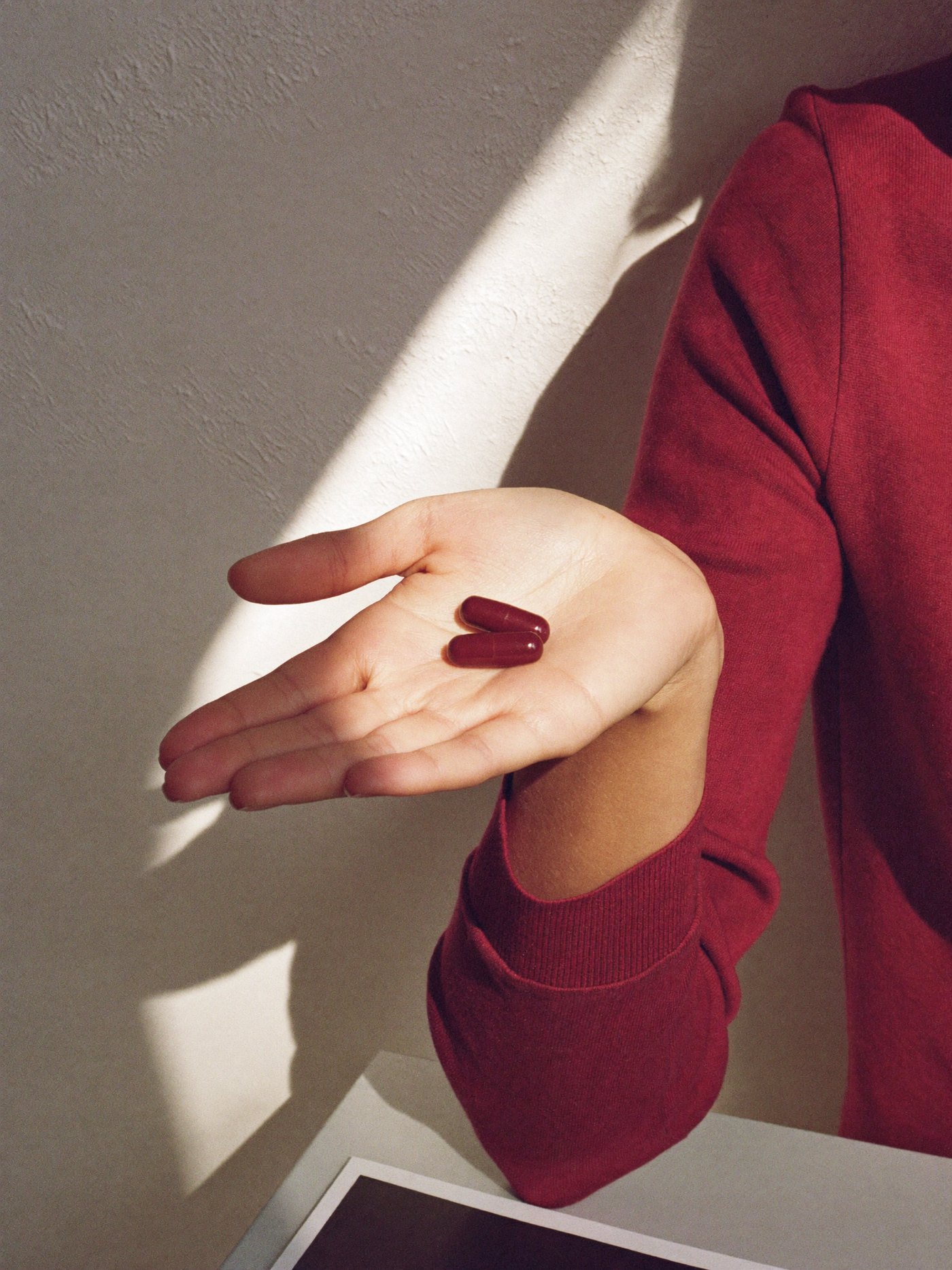 Two maroon capsules resting in an open palm in soft light.