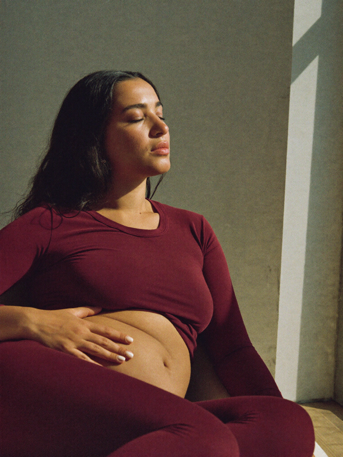 A woman at ease in warm light, hand resting on her stomach.